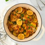 Lemon roasted chicken in a dutch oven over on a white countertop with lemons ready to enjoy