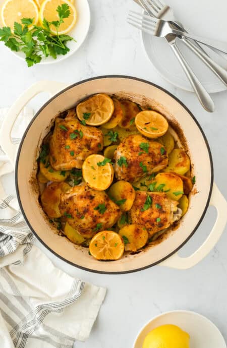 Lemon roasted chicken in a dutch oven over on a white countertop with lemons ready to enjoy