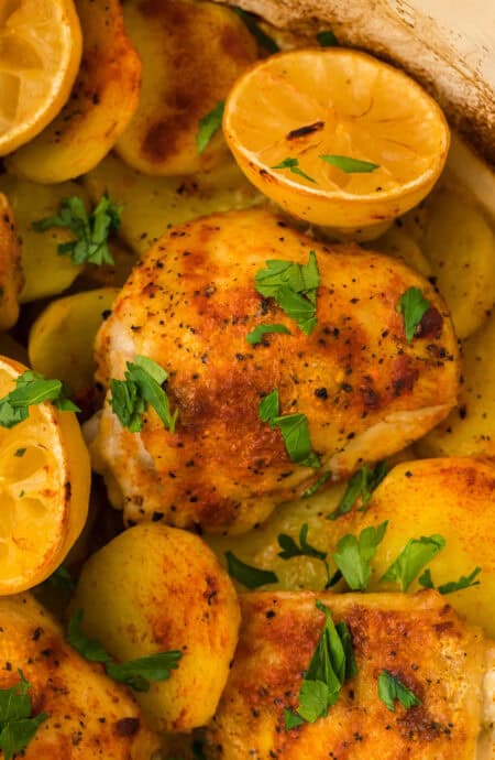 A close up of lemon roast chicken in a dutch oven with lemon halves ready to serve