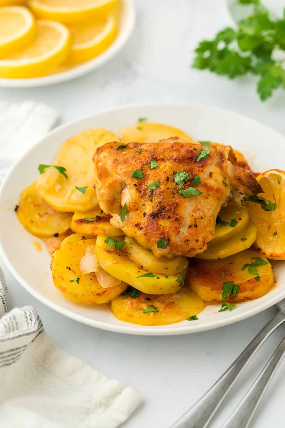 Roasted chicken with lemon and potatoes on a white plate with lemons in the background