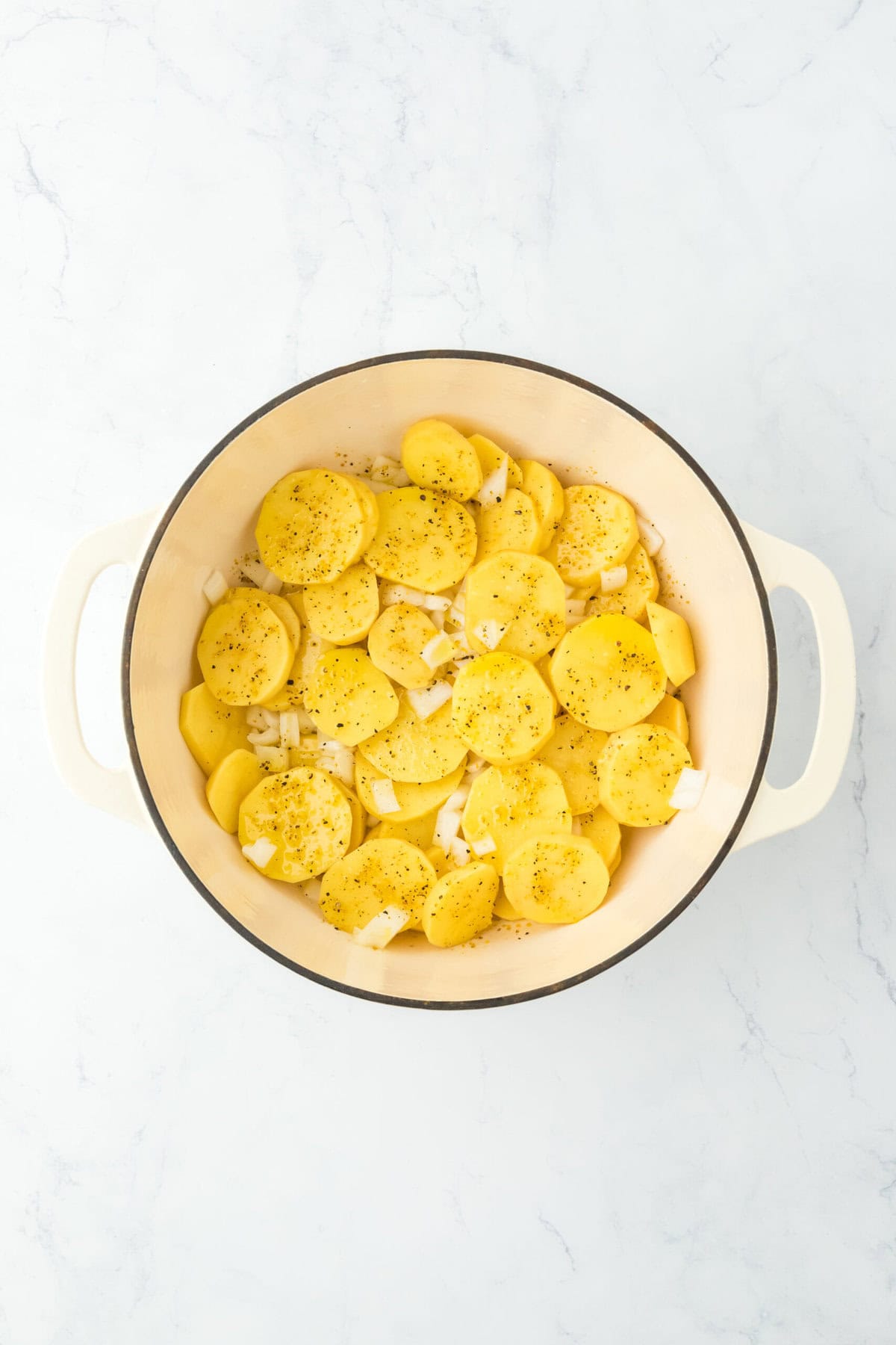 Potato slices and onions in dutch oven on white countertop