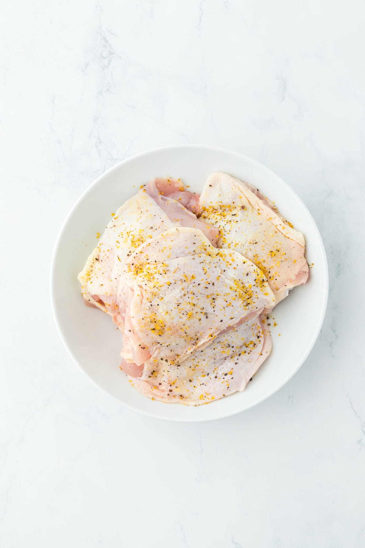 Chicken pieces on a white plate seasoned on white countertop