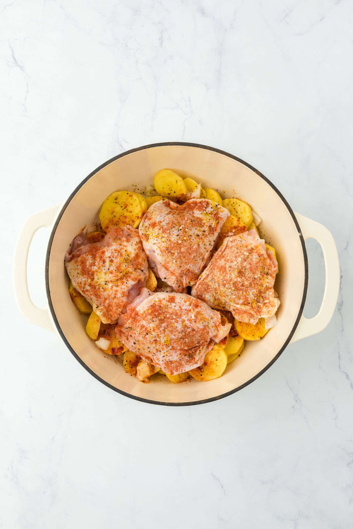 Seasoned chicken pieces on potatoes and onions in a dutch oven