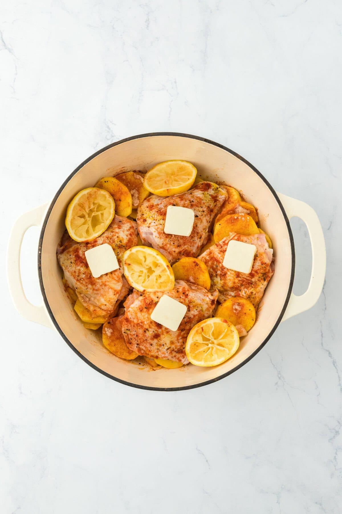 Seasoned chicken on potatoes with butter and lemons in dutch oven