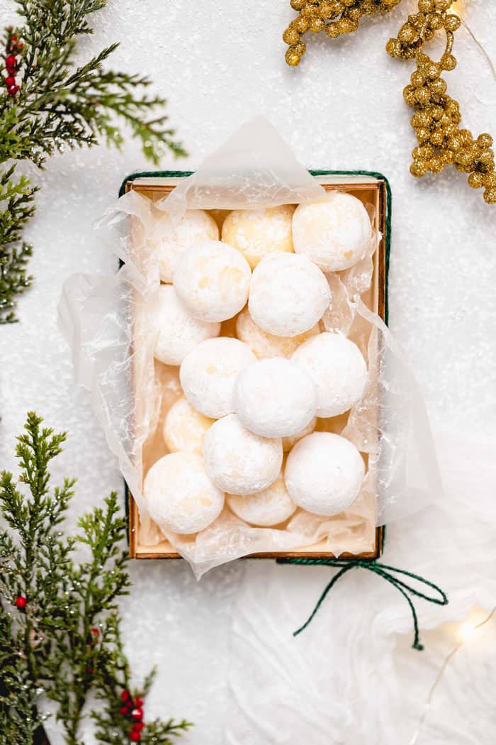 white chocolate truffles in a holiday box against a white background with holly and green leaves