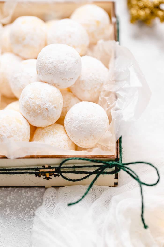 A beige box with green ribbon tied in a bow filled with orange truffles for the holidays