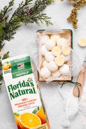 A box of truffles against a white background with orange juice carton and christmas branches
