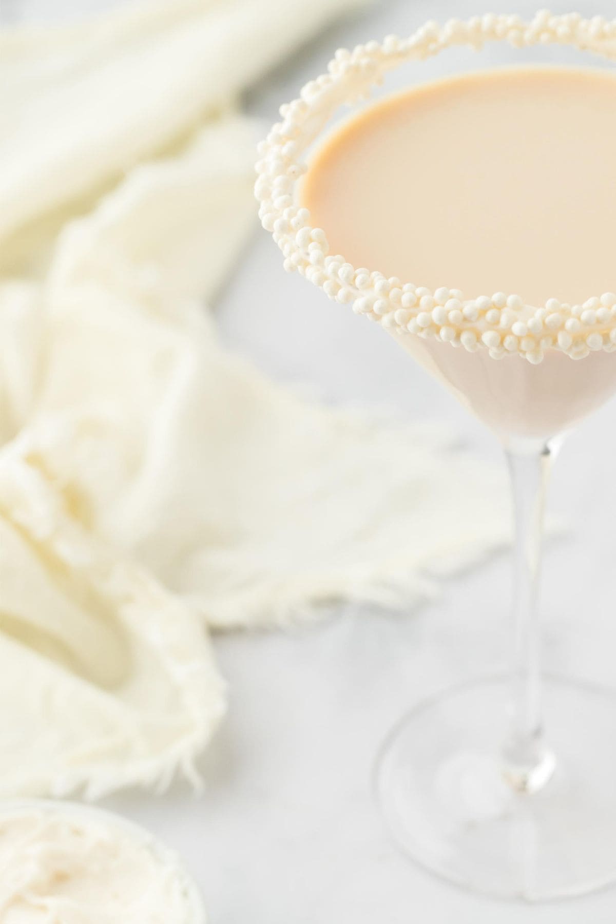 A close-up of a martini glass with a pearl-sprinkled rim, filled with sugar cookie martini