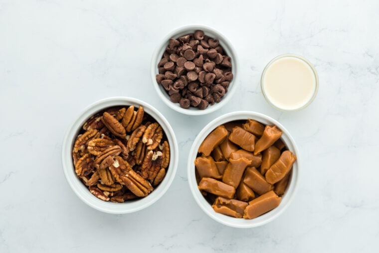 Pecans, chocolate, caramel in white bowls on white countertop