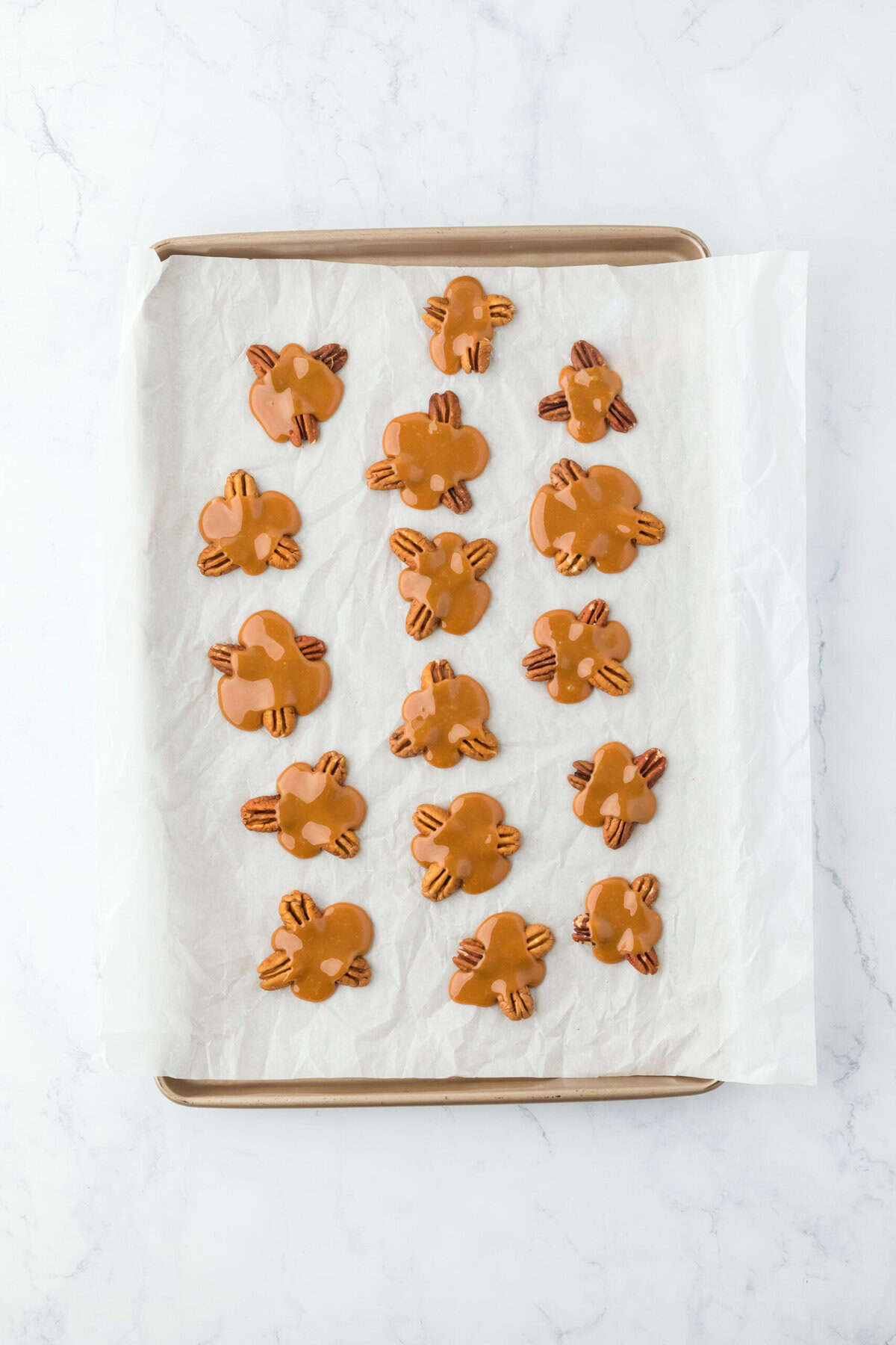 Caramel spooned over groups of pecans on white parchment.