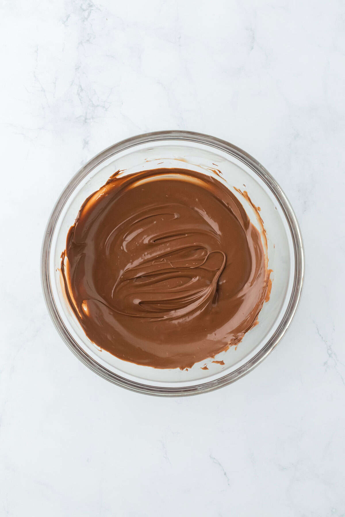 Melted chocolate in a glass bowl on white countertop.