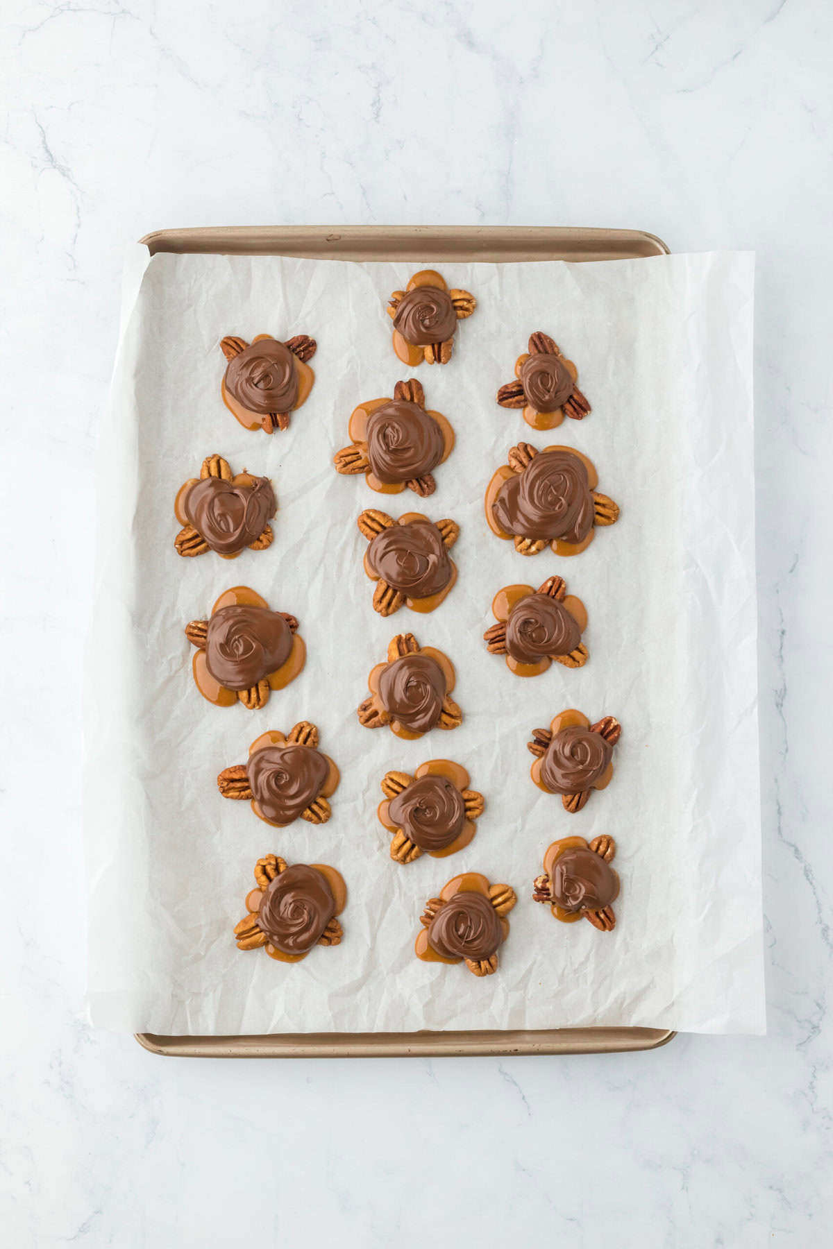 Completed turtle chocolate candies on a parchment lined baking sheet