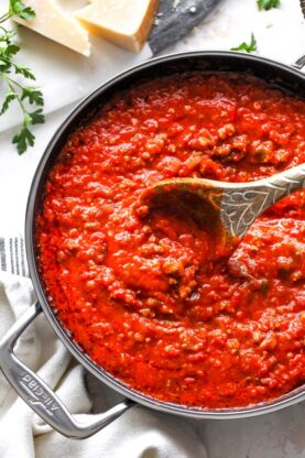 A delicious sausage tomato sauce is being stirred with a wooden spoon in a large pot