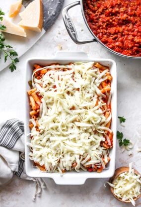 Delicious ziti pasta in a white baking dish with shredded cheese on top before putting in the oven
