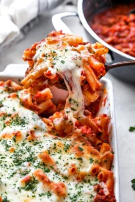 Baked ziti being lifted from white pan after being baked
