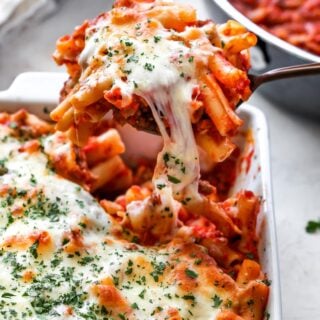 Baked ziti being lifted from white pan after being baked