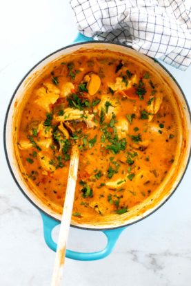 A large blue pot filled with just cooked moqueca with a wooden spoon ready to serve