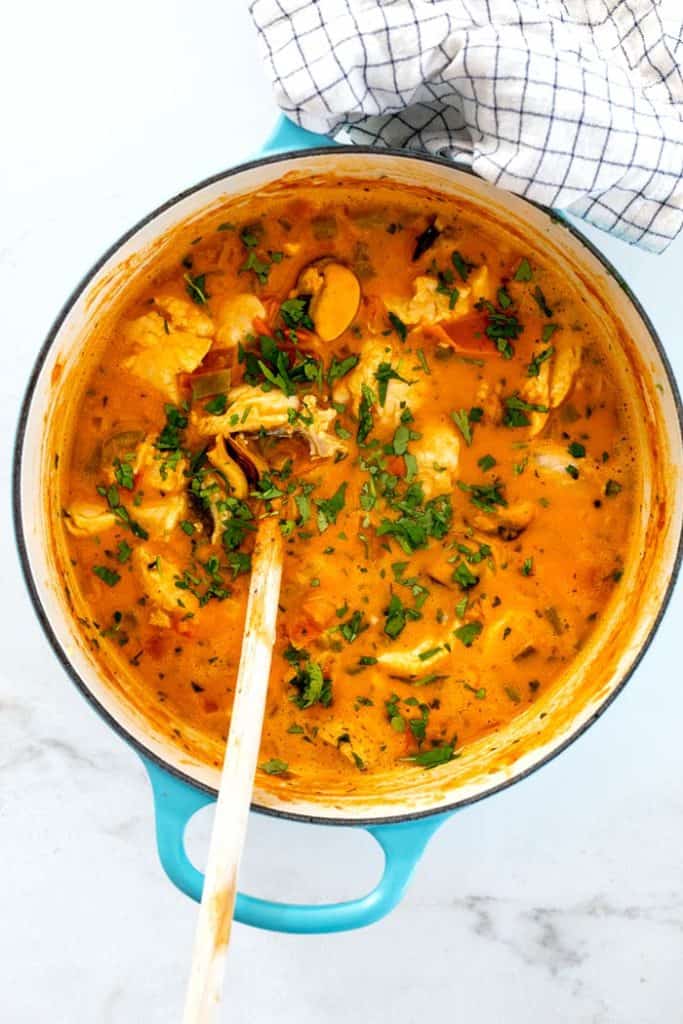 A large blue pot filled with just cooked moqueca with a wooden spoon ready to serve