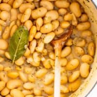 A close up of baby lima beans stewing in a pot with a wooden spoon