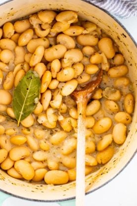 A close up of baby lima beans stewing in a pot with a wooden spoon 