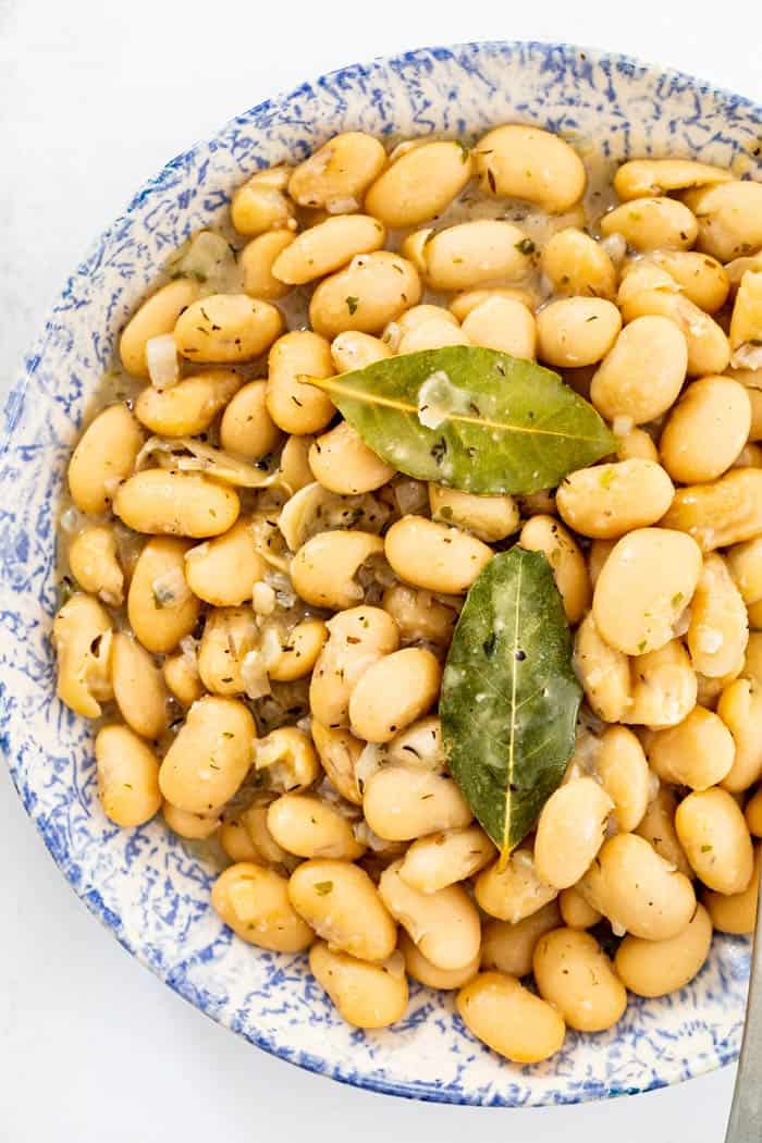 A large blue and white patterned bowl filled with creamy Southern butter beans with two bay leaves on top