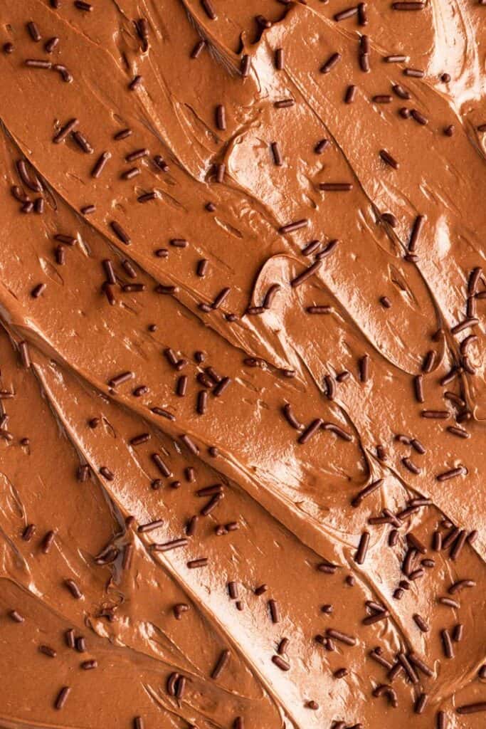 A close up of chocolate buttercream spread on a sheet cake with chocolate sprinkles