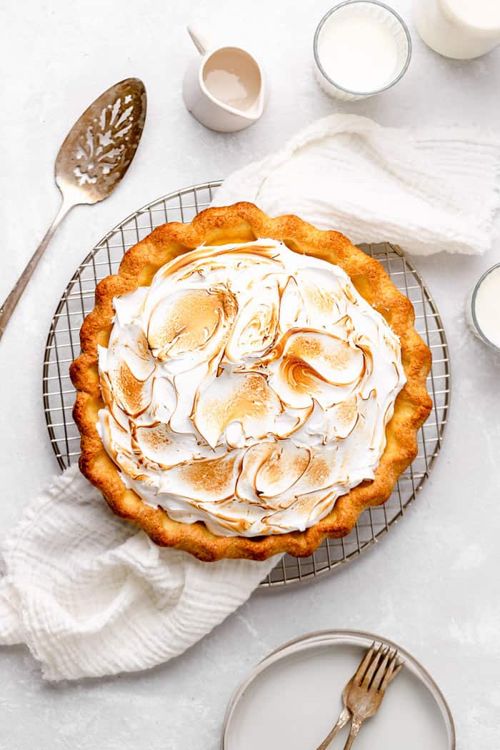 A overhead image of a just baked lemon meringue pie against a white background with a pie server and white napkin
