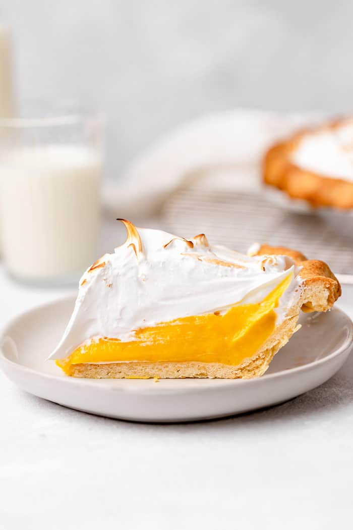 A perfect slice of a lemon curd filled pie with meringue topping on a white plate against white background