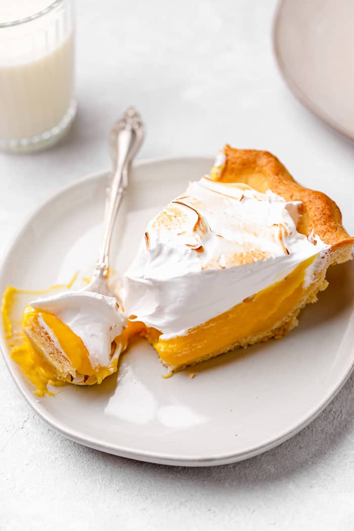 A slice of lemon pie being eaten with a silver fork on a white plate