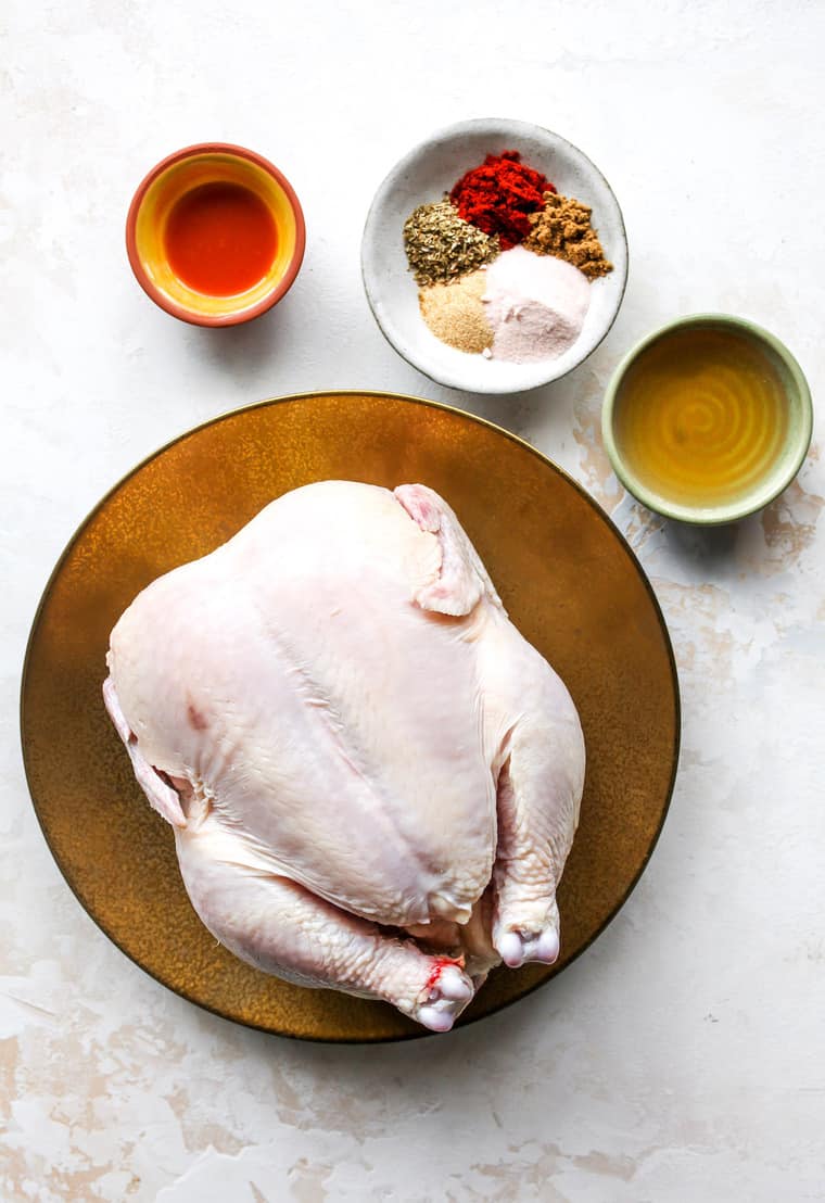 Ingredients for roast chicken including a whole chicken and spices in bowls