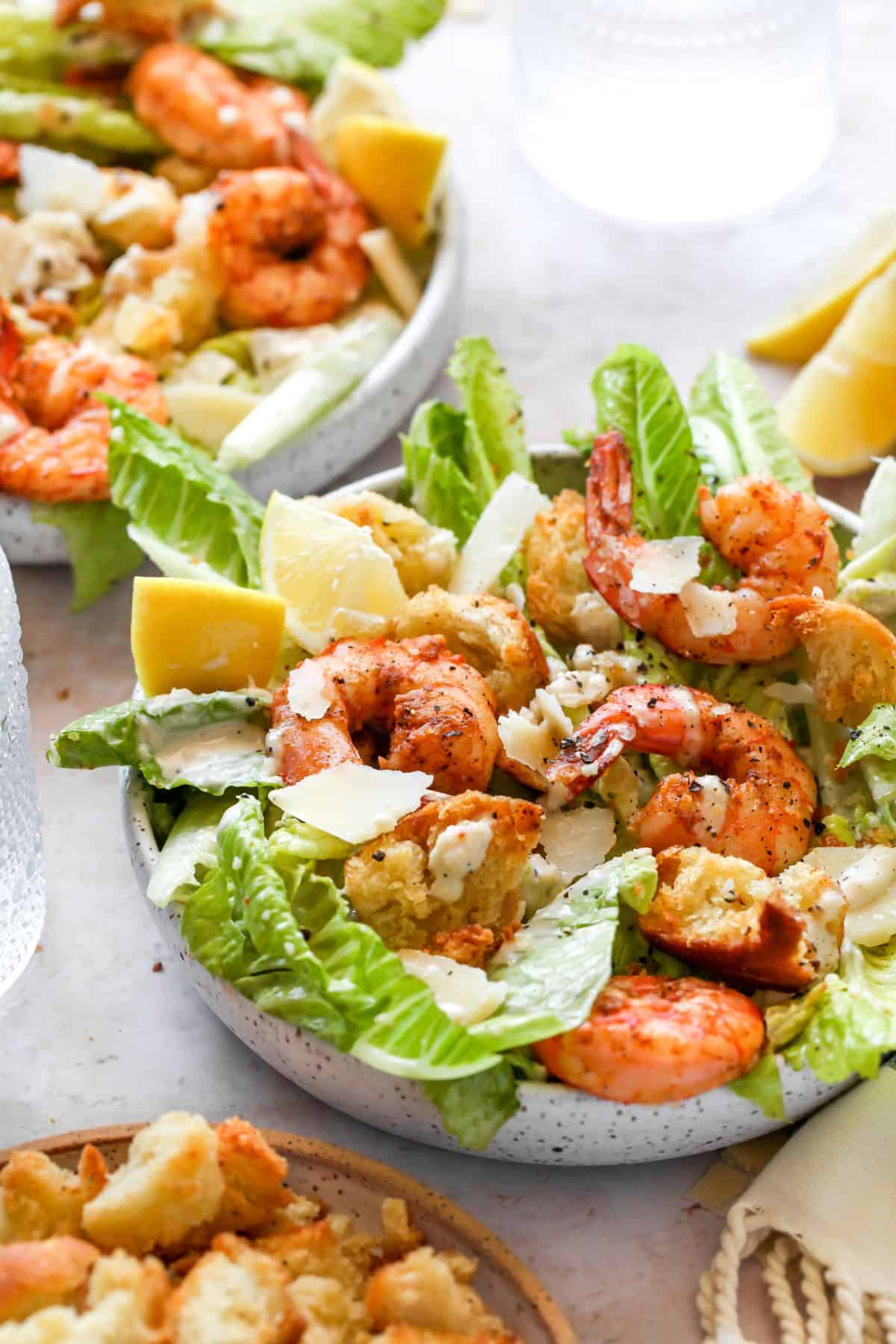 Caesar salad loaded with shrimp, croutons, and shaved parmesan, served in a ceramic bowl with lemon wedges