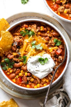 A close up of taco soup in large white bowl with cheese and sour cream with tortilla chips