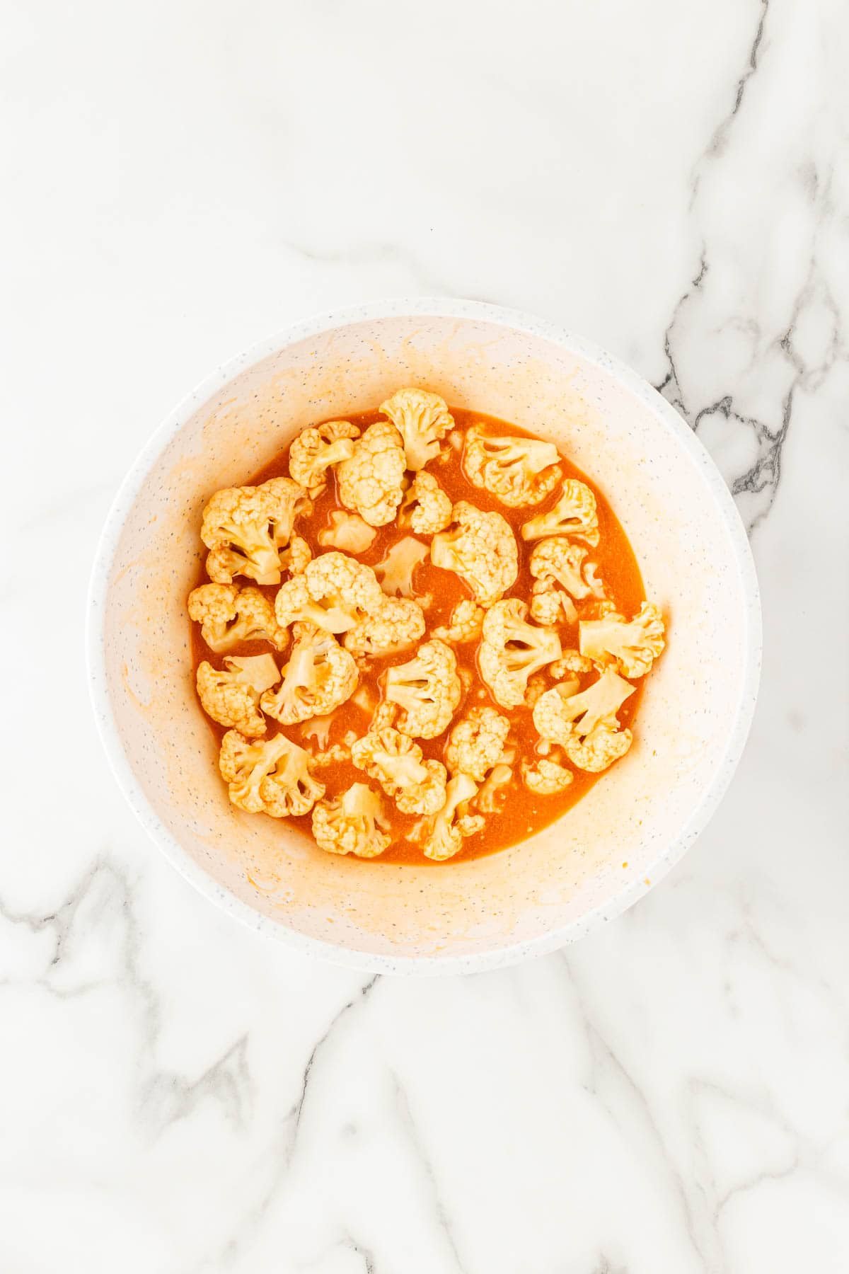 Raw cauliflower florets soaking in buttermilk marinade in a bowl