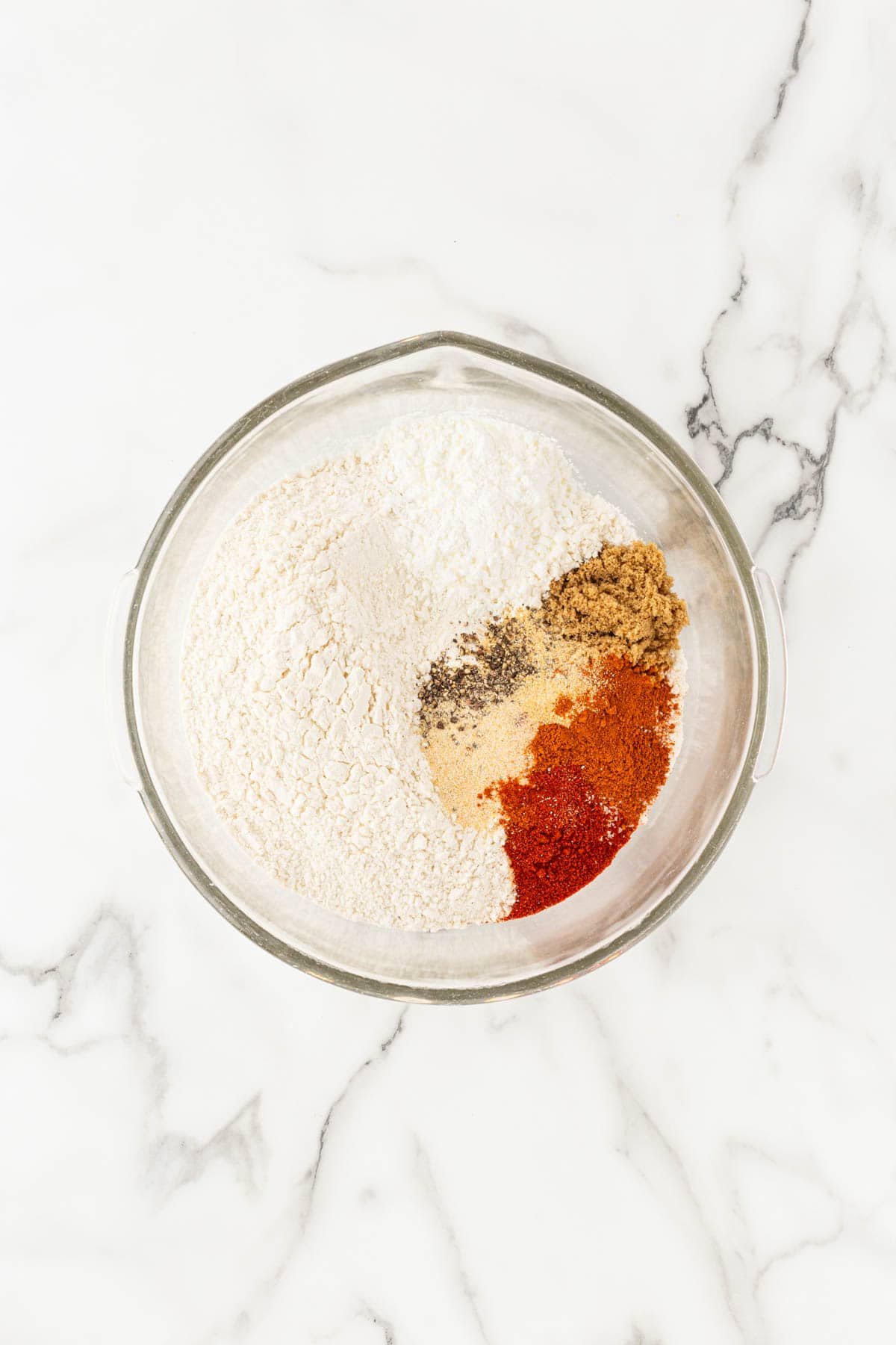 Closeup of flour and spices mixed together in a bowl on a marble countertop