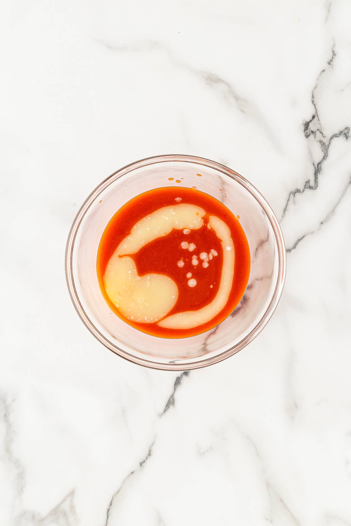 Buffalo sauce mixture with melted butter in a clear bowl on a marble counter