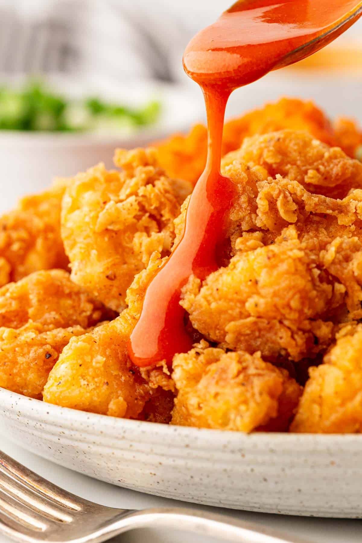 Buffalo sauce being drizzled over a plate of fried cauliflower