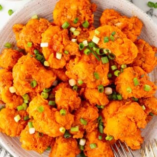 A plate piled with buffalo fried cauliflower topped with sliced green onions, with dipping sauce nearby