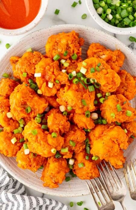 A plate piled with buffalo fried cauliflower topped with sliced green onions, with dipping sauce nearby