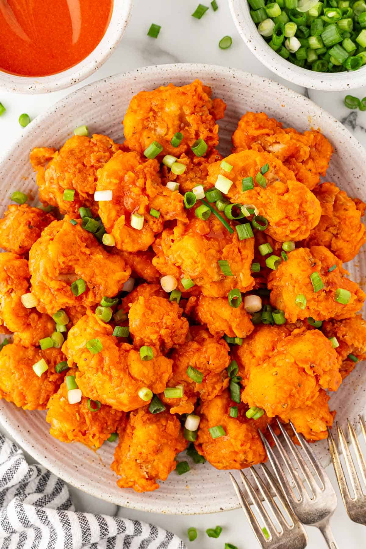 A plate piled with buffalo fried cauliflower topped with sliced green onions, with dipping sauce nearby