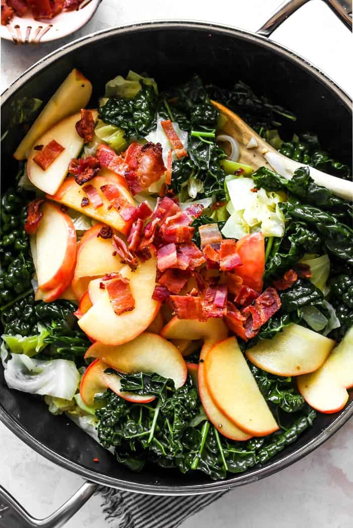 Apple slices, bacon, cabbage and kale in a pan being braised