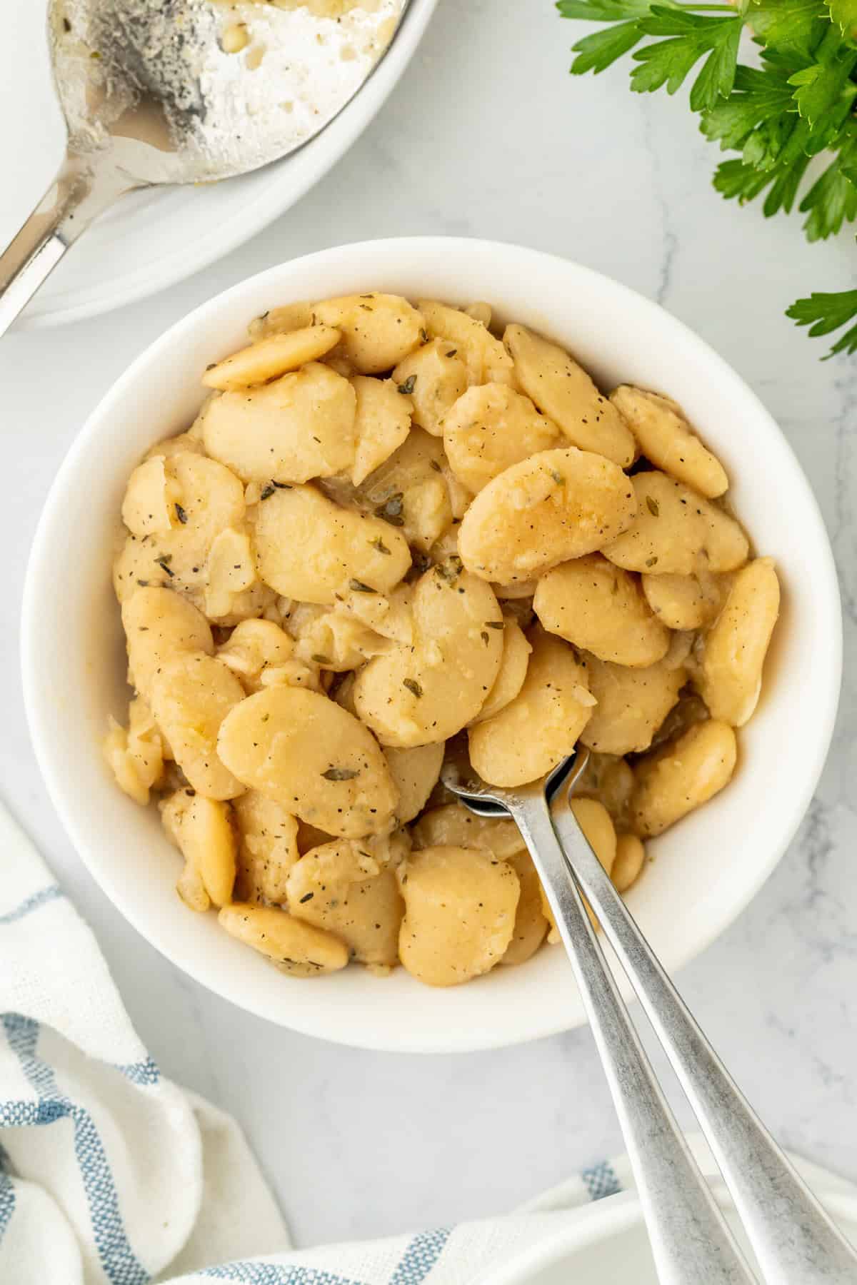A small bowl of the best butter beans recipe with a silver spoon digging in on a white background