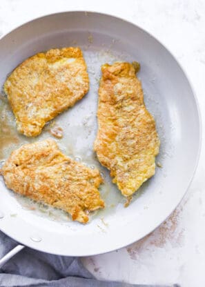 Egg battered thin chicken breasts frying in pan