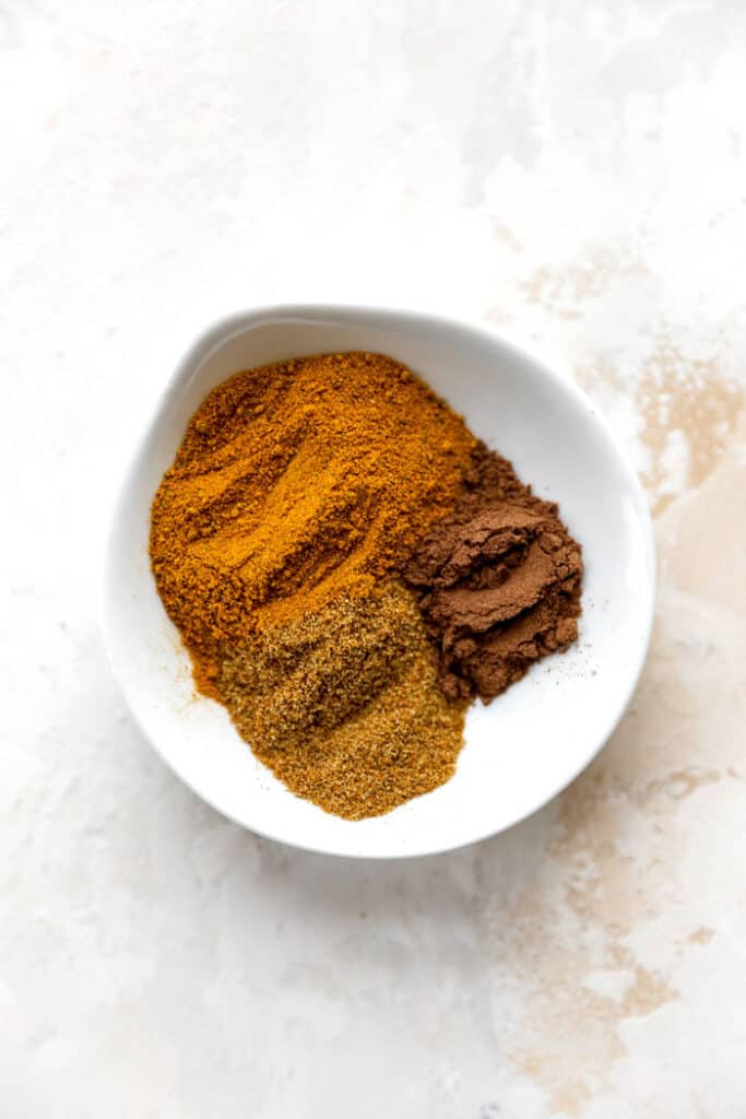 A white bowl filled with curry powder, allspice and cumin