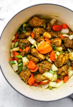 Curry chicken in a large pot with peppers, onions and scotch pepper