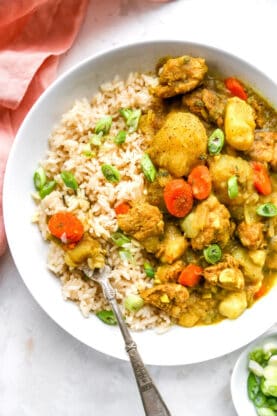 A delicious curry stew filled with chicken and potatoes in a white bowl with rice ready to enjoy