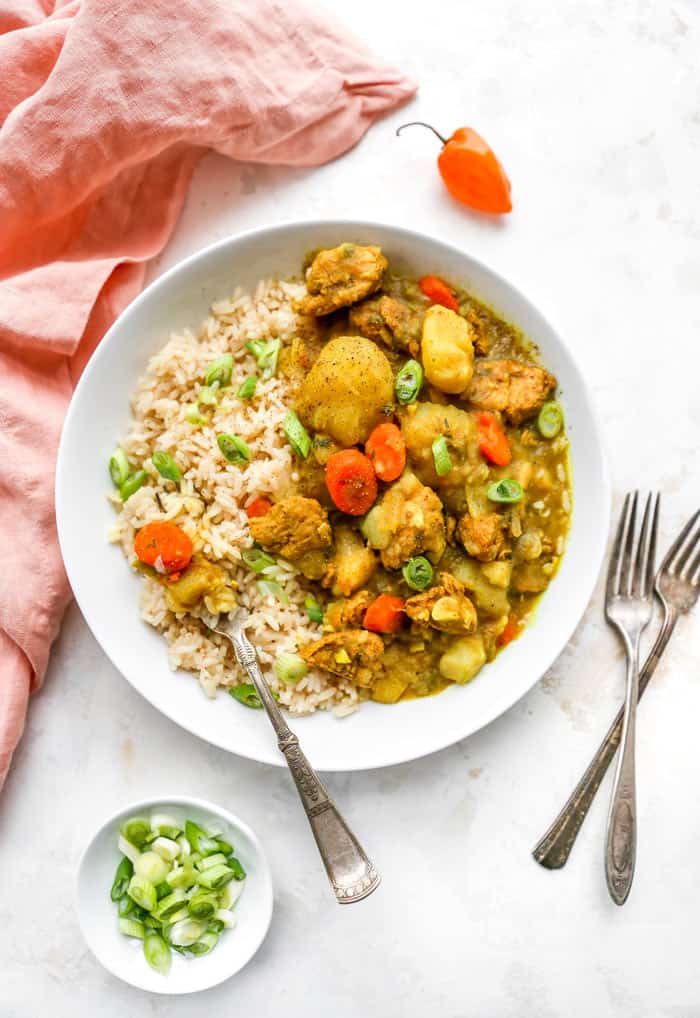 A delicious curry stew filled with chicken and potatoes in a white bowl with rice ready to enjoy against a white background with coral napkin