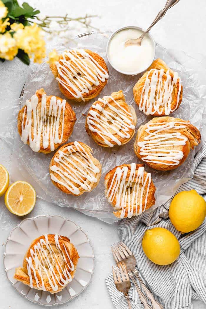 Several lemon cinnamon rolls against a white background with whole lemons and flowers