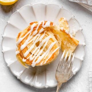 A lemon cinnamon roll biscuit on a white plate with fork opening the inside of the flaky dough