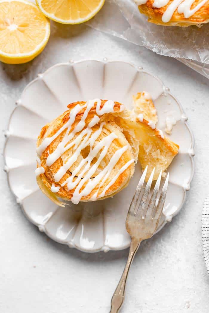 A lemon cinnamon roll biscuit on a white plate with fork opening the inside of the flaky dough