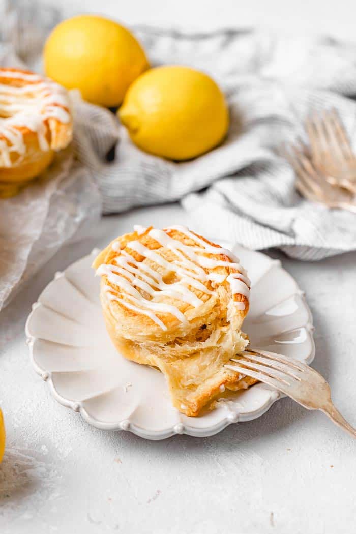 Several lemon cinnamon rolls with one in the center on a white plate being opened with a fork